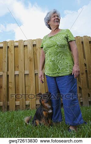 Low angle view of a senior woman standing with a dog in a lawn and smiling View Large Photo Image Stock Image - Low angle view of a senior woman standing with a dog in a lawn and smiling. Fotosearch