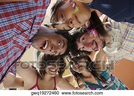 Stock Image - Low angle view of five friends standing in a huddle and smiling. Fotosearch