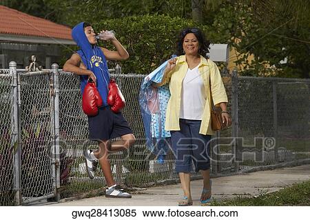 Mature woman walking with a teenage boy leaning on a chain-link fence and drinking water beside her View Large Photo Image Stock Photography - Mature woman walking with a teenage boy leaning on a chain-link fence and drinking water beside her. Fotosearch