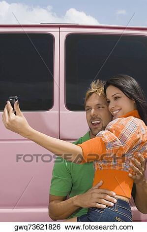 Stock Photograph - Mid adult man and a young woman taking a photograph of themselves. Fotosearch