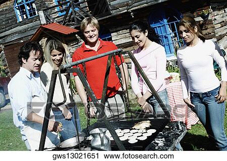 Mid adult man preparing food in a barbecue grill with four people standing beside him View Large Photo Image Stock Image - Mid adult man preparing food in a barbecue grill with four people standing beside him. Fotosearch