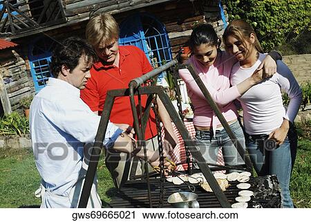 Mid adult man preparing food in a barbecue grill with three people standing beside him View Large Photo Image Stock Image - Mid adult man preparing food in a barbecue grill with three people standing beside him. Fotosearch