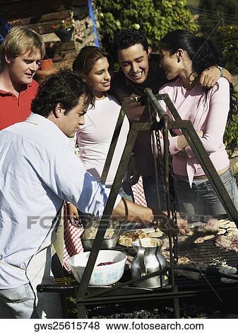 Mid adult man preparing food in a barbecue grill with four people standing beside him View Large Photo Image Stock Photo - Mid adult man preparing food in a barbecue grill with four people standing beside him. Fotosearch