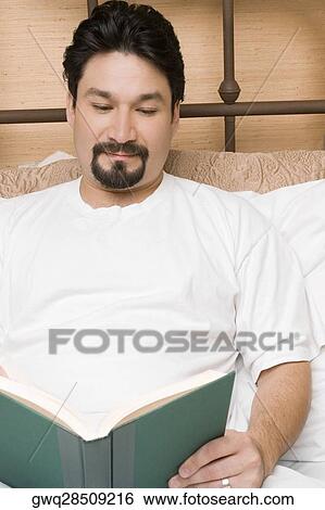 Mid adult man reclining on the bed and reading a book View Large Photo Image Stock Photograph - Mid adult man reclining on the bed and reading a book. Fotosearch