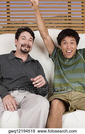 Mid adult man sitting on a couch with a young man and smiling View Large Photo Image Stock Photo - Mid adult man sitting on a couch with a young man and smiling. Fotosearch
