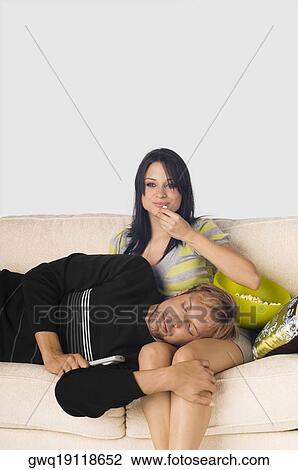 Stock Image - Mid adult man sleeping on the lap of a young woman eating popcorns. Fotosearch