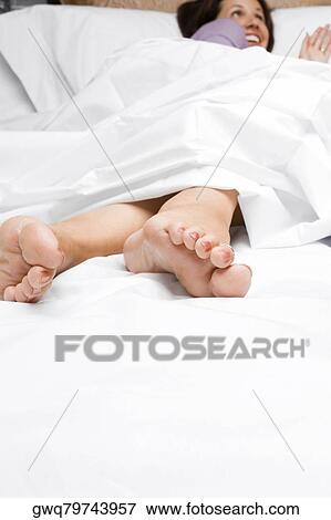 Stock Photo - Mid adult woman lying on the bed and smiling. Fotosearch