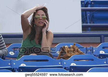 Stock Photo - Mid adult woman sitting on bleachers and talking on a mobile phone. Fotosearch