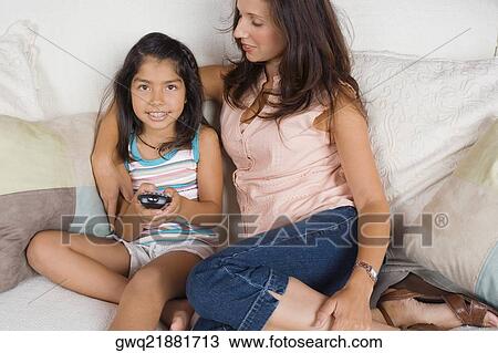 Stock Image - Mid adult woman sitting with her daughter on a couch. Fotosearch