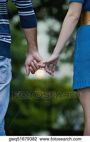 Stock Image - Mid section view of a couple holding hands of each other and walking. Fotosearch