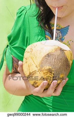 Picture - Mid section view of a young woman drinking coconut milk with a drinking straw. Fotosearch
