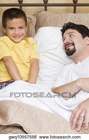 Portrait of a boy sitting on the bed with his father looking at him View Large Photo Image Stock Photograph - Portrait of a boy sitting on the bed with his father looking at him. Fotosearch