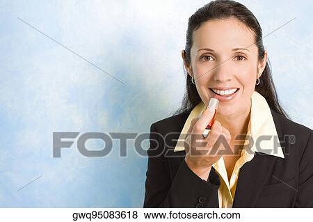 Stock Photo - Portrait of a businesswoman applying lipstick on her lips. Fotosearch