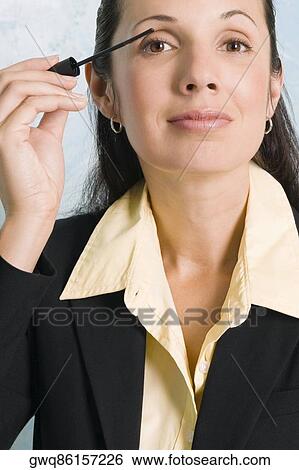 Stock Photograph - Portrait of a businesswoman applying mascara on her eyes. Fotosearch