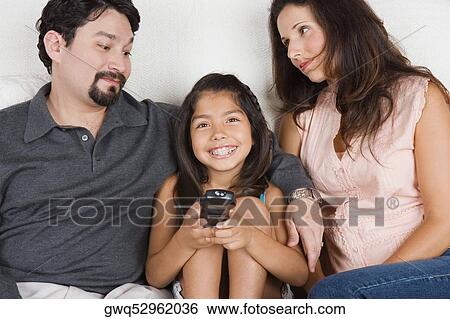 Portrait of a girl holding a remote control with her parents sitting beside her View Large Photo Image Stock Photograph - Portrait of a girl holding a remote control with her parents sitting beside her. Fotosearch