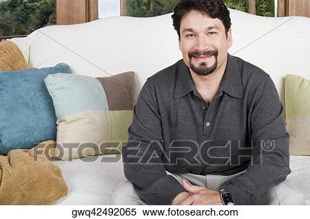 Portrait of a mid adult man sitting on a couch and smirking View Large Photo Image Stock Photography - Portrait of a mid adult man sitting on a couch and smirking. Fotosearch