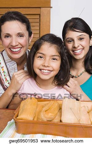 Portrait of a mid adult woman and her two daughters smiling with a tray of breads in the kitchen View Large Photo Image Stock Image - Portrait of a mid adult woman and her two daughters smiling with a tray of breads in the kitchen. Fotosearch