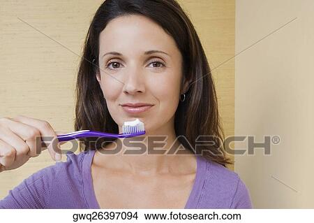 Portrait of a mid adult woman holding a toothbrush in front of her mouth View Large Photo Image Picture - Portrait of a mid adult woman holding a toothbrush in front of her mouth. Fotosearch