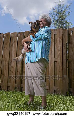 Stock Photo - Portrait of a senior woman carrying a dog. Fotosearch