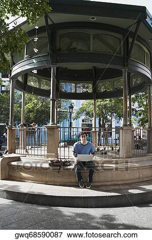 Portrait of a young man sitting and using a laptop View Large Photo Image Stock Photo - Portrait of a young man sitting and using a laptop. Fotosearch