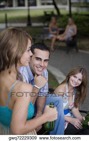Portrait of a young man sitting between two young women and smiling View Large Photo Image Stock Photo - Portrait of a young man sitting between two young women and smiling. Fotosearch