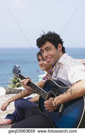 Stock Photo - Portrait of a young man sitting with a young woman and playing a guitar. Fotosearch