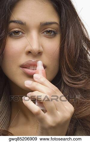 Portrait of a young woman applying lip gloss View Large Photo Image Stock Photo - Portrait of a young woman applying lip gloss. Fotosearch