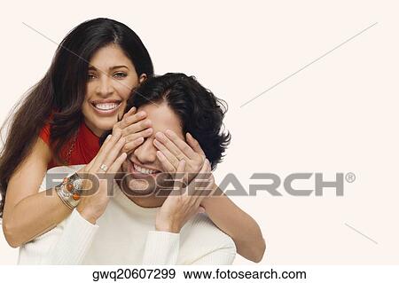 Stock Photo - Portrait of a young woman covering eyes of a young man from behind. Fotosearch