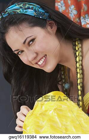 Picture - Portrait of a young woman holding a packet of potato chips. Fotosearch