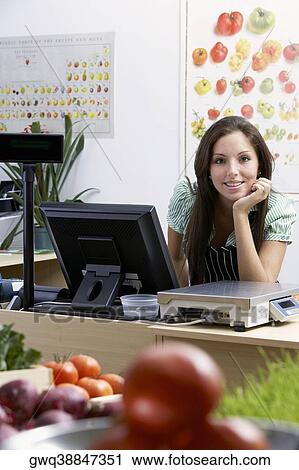 Stock Image - Portrait of a young woman leaning at a checkout counter and smiling. Fotosearch