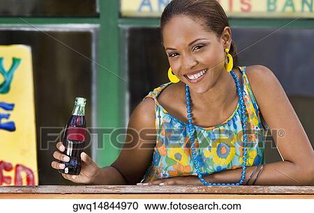 Portrait of a young woman leaning on a railing and holding a cola bottle View Large Photo Image Stock Image - Portrait of a young woman leaning on a railing and holding a cola bottle. Fotosearch