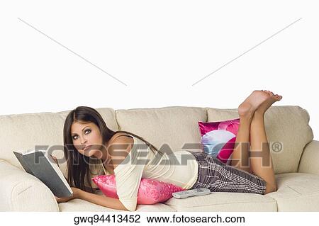 Portrait of a young woman lying on a couch and holding a book View Large Photo Image Stock Image - Portrait of a young woman lying on a couch and holding a book. Fotosearch