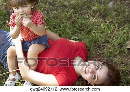 Portrait of a young woman lying on grass with her daughter sitting on her stomach View Large Photo Image Stock Image - Portrait of a young woman lying on grass with her daughter sitting on her stomach. Fotosearch
