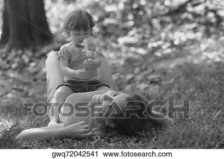 Portrait of a young woman lying on grass with her daughter sitting on her stomach View Large Photo Image Stock Image - Portrait of a young woman lying on grass with her daughter sitting on her stomach. Fotosearch