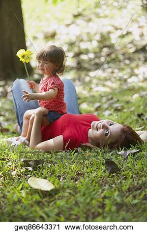 Portrait of a young woman lying on grass with her daughter sitting on her stomach View Large Photo Image Stock Image - Portrait of a young woman lying on grass with her daughter sitting on her stomach. Fotosearch