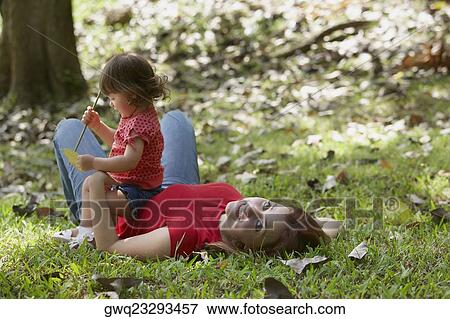 Portrait of a young woman lying on grass with her daughter sitting on her stomach View Large Photo Image Stock Photo - Portrait of a young woman lying on grass with her daughter sitting on her stomach. Fotosearch