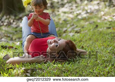 Portrait of a young woman lying on grass with her daughter sitting on her stomach View Large Photo Image Stock Photo - Portrait of a young woman lying on grass with her daughter sitting on her stomach. Fotosearch