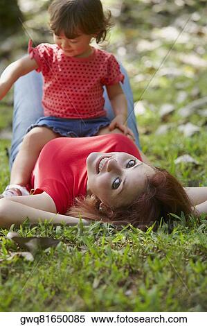 Portrait of a young woman lying on grass with her daughter sitting on her stomach View Large Photo Image Stock Photography - Portrait of a young woman lying on grass with her daughter sitting on her stomach. Fotosearch
