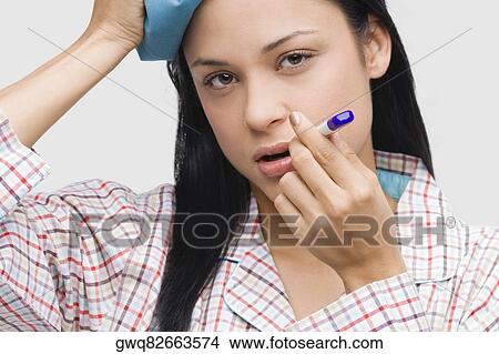 Portrait of a young woman measuring her temperature with a thermometer and holding an ice pack on her head View Large Photo Image Picture - Portrait of a young woman measuring her temperature with a thermometer and holding an ice pack on her head. Fotosearch