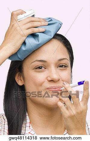 Portrait of a young woman measuring her temperature with a thermometer and holding an ice pack on her head View Large Photo Image Stock Photo - Portrait of a young woman measuring her temperature with a thermometer and holding an ice pack on her head. Fotosearch