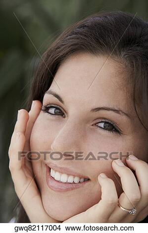 Portrait of a young woman smiling with her hands on her chin View Large Photo Image Picture - Portrait of a young woman smiling with her hands on her chin. Fotosearch