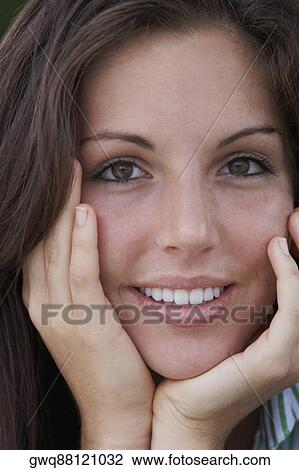 Portrait of a young woman smiling with her hands on her chin View Large Photo Image Stock Image - Portrait of a young woman smiling with her hands on her chin. Fotosearch