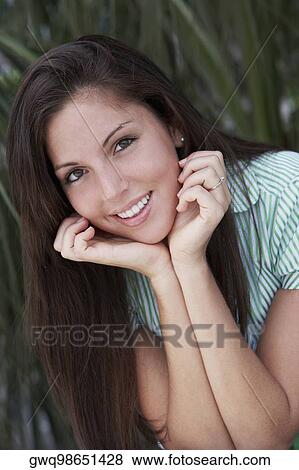 Portrait of a young woman smiling with her hands on her chin View Large Photo Image Stock Photo - Portrait of a young woman smiling with her hands on her chin. Fotosearch
