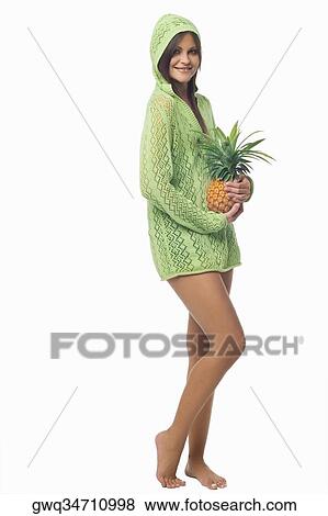 Stock Photo - Portrait of a young woman standing and holding a pineapple. Fotosearch