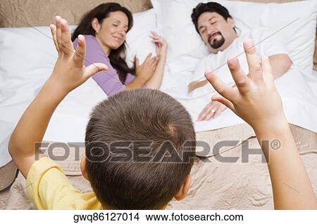 Rear view of a boy gesturing at his parents sleeping on the bed View Large Photo Image Picture - Rear view of a boy gesturing at his parents sleeping on the bed. Fotosearch
