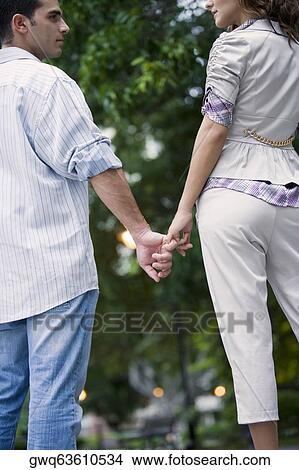 Rear view of a young couple holding hands of each other View Large Photo Image Picture - Rear view of a young couple holding hands of each other. Fotosearch