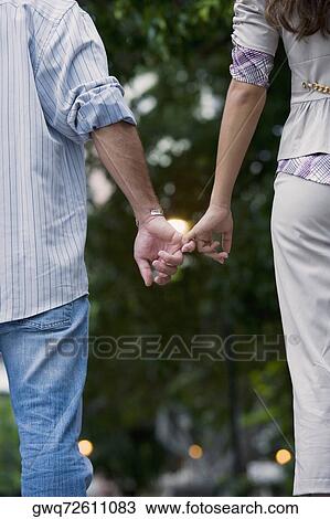 Rear view of a young couple holding hands of each other View Large Photo Image Stock Image - Rear view of a young couple holding hands of each other. Fotosearch