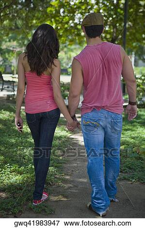 Rear view of a young couple holding hands of each other and walking in a park View Large Photo Image Stock Photo - Rear view of a young couple holding hands of each other and walking in a park. Fotosearch