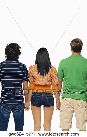 Stock Image - Rear view of a young woman and two men standing with holding their hands. Fotosearch