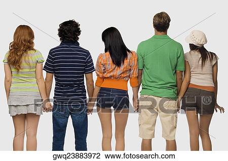 Stock Image - Rear view of two men and three young women standing with holding their hands. Fotosearch